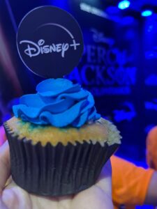 cupcake com glacê azul no topo e um palitinho com a logo do Disney Plys em cima. A luz azul ilumina a foto.