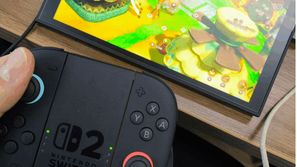 Imagem do Nintendo Switch 2, controles soltos apoiados no suporte de Joystick e console na mesa com um jogo